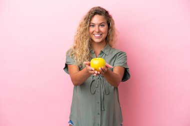 Kıvırcık saçlı kız pembe arka planda izole edilmiş hamile ve elinde elma var.