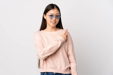 İzole edilmiş beyaz arka planı olan genç bir Çinli kız bir ürün sunmak için kenarı işaret ediyor.