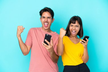 Mavi arka planda cep telefonu tutan genç melez çift zaferi kutluyor.