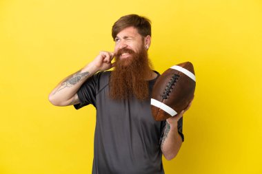 Kızıl saçlı beyaz adam sarı arka planda ragbi oynuyor. 