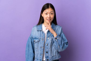 Soyutlanmış mor arka planda genç bir Çinli kız sessizce hareket ettiğini gösteriyor. Parmağını ağzına sok.