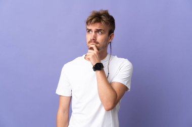Genç yakışıklı sarışın adam, mor arka planda izole edilmiş. Şüpheleri ve düşünceleri var.