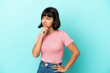 Genç melez kadın mavi arka planda izole edilmiş kuşkuları var.