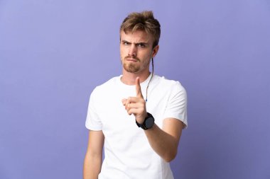 Mor arka planda izole edilmiş genç sarışın adam hayal kırıklığına uğramış ve ön tarafı işaret ediyor.
