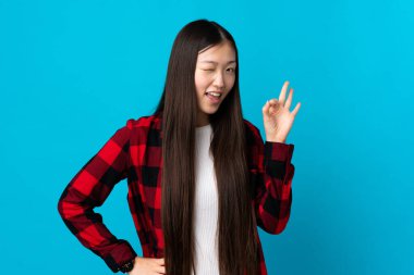 İzole edilmiş mavi arka planda genç bir Çinli kız parmaklarıyla işaret veriyor.
