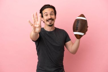 Pembe arka planda ragbi oynayan genç beyaz adam mutlu ve parmaklarıyla dört kişi sayıyor.