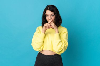Mavi arka planda izole edilmiş genç Ukraynalı kız sessizlik işareti gösteriyor.