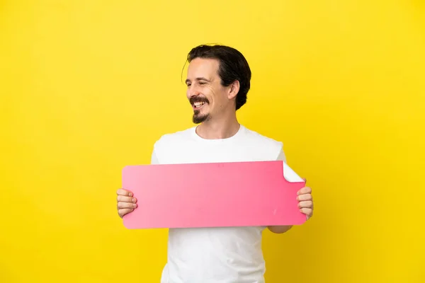 Jovem Caucasiano Isolado Fundo Amarelo Segurando Cartaz Vazio Olhando Para — Fotografia de Stock