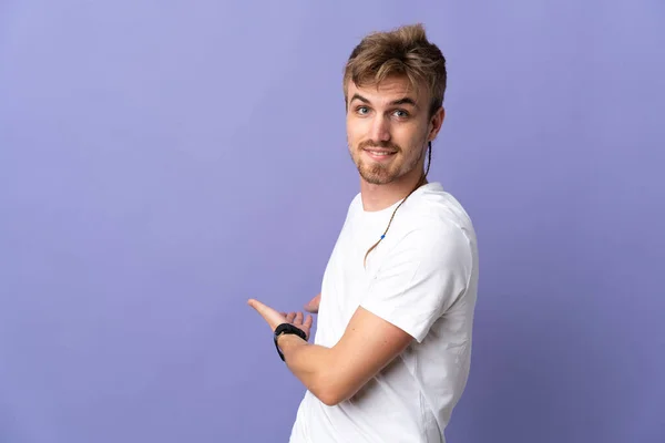 Mladý Pohledný Blondýnka Muž Izolovaný Fialové Pozadí Natahuje Ruce Strany — Stock fotografie