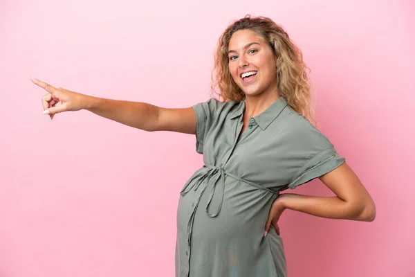 妊娠中や横を指してピンクの背景に隔離された巻き毛の女の子 — ストック写真
