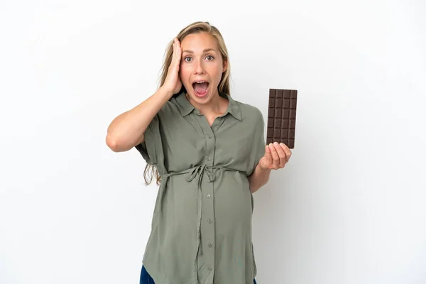 白い背景に孤立した若い白人女性妊娠中のチョコレートを持っていると驚きの表情 — ストック写真
