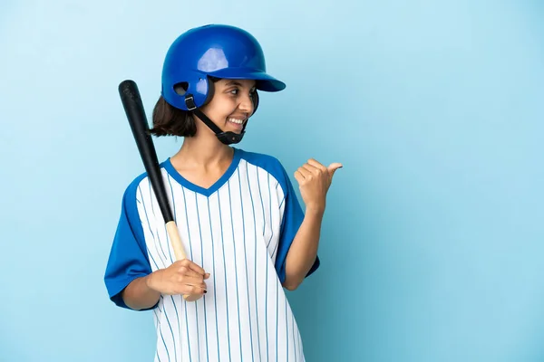 棒球混合赛选手妇女与安全帽和球棒隔离蓝色背景指向侧面介绍产品 — 图库照片