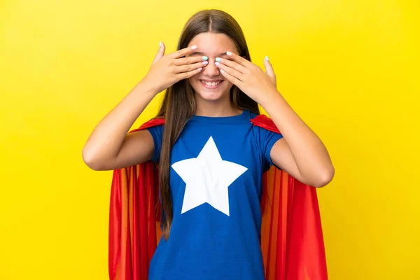 小さなCaucasianスーパーヒーロー女の子絶縁上の黄色背景カバー目によって手 — ストック写真