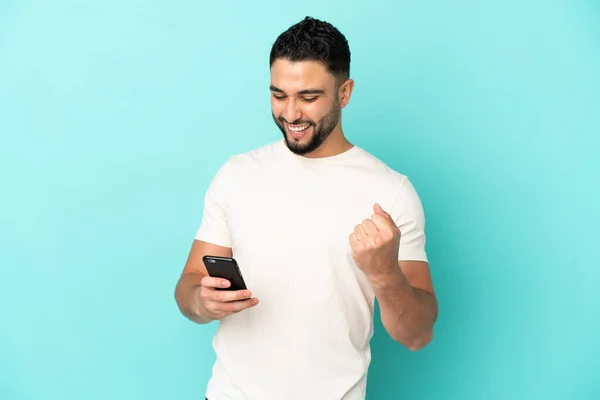 Hombre Árabe Joven Aislado Sobre Fondo Azul Con Teléfono Posición —  Fotos de Stock