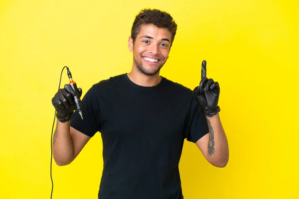 タトゥーアーティストブラジル人男性は黄色の背景に孤立素晴らしいアイデアを指摘 — ストック写真