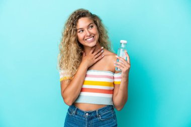 Mavi arka planda bir şişe suyu olan genç sarışın kadın gülümserken yukarı bakıyor.