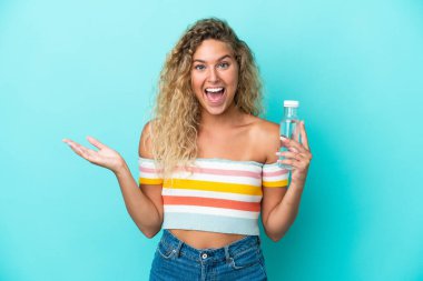 Mavi arka planda su şişesi olan genç sarışın kadın şok olmuş yüz ifadesi ile izole edilmiş.