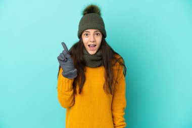 Mavi arka planda izole edilmiş genç bir Fransız kız. Kış şapkasıyla çözümü bulmak için parmağını kaldırıyor.