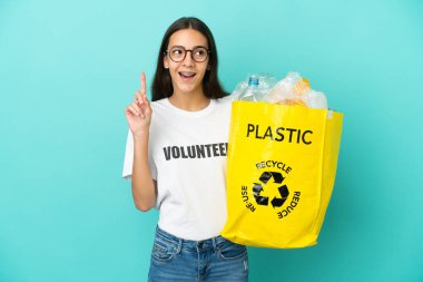 Elinde plastik şişelerle dolu bir çanta tutan genç bir Fransız kızı geri dönüşüm için parmağıyla işaret eden bir fikir düşünüyor.