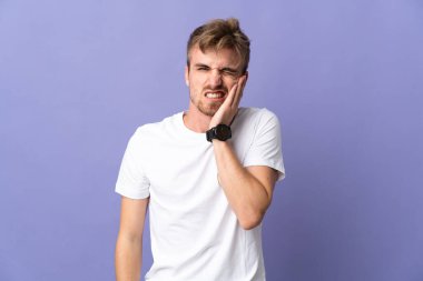 Mor arka planda dişleri ağrıyan yakışıklı sarışın bir adam.