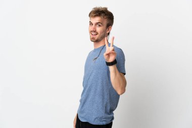 Beyaz arka planda izole edilmiş yakışıklı genç adam gülümsüyor ve zafer işareti gösteriyor