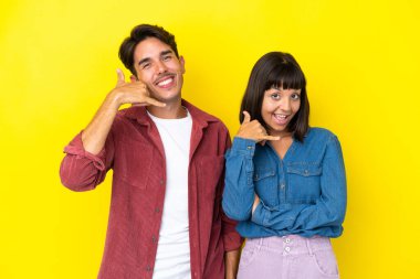 Sarı arka planda izole edilmiş genç melez bir çift telefon jesti yapıyor. Bana geri dönüş işareti ver.