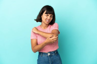 Genç melez kadın, mavi arka planda soyutlanmış, dirseğinde ağrı var.