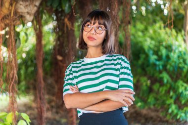 Parkta genç esmer bir kadın gülümserken yukarı bakıyor.