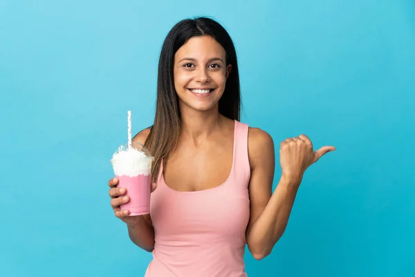 イチゴミルクセーキを持つ若い女性が製品を提示する側を指している — ストック写真