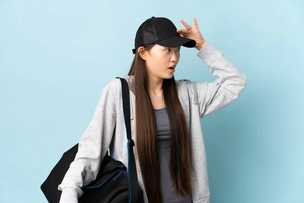 年轻的中国女运动员 头戴运动包 蓝色孤立的背景 满脸惊讶的表情 环顾四周 — 图库照片