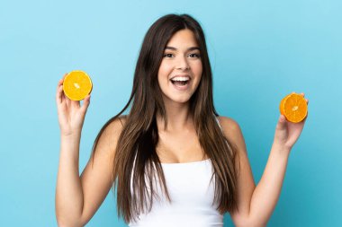 İzole edilmiş mavi arka planı olan Brezilyalı genç bir kız elinde portakal tutuyor.