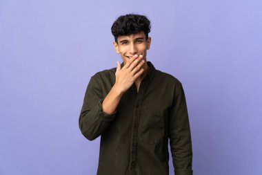 Arjantinli genç adam arka planda izole edilmiş mutlu ve gülümseyen ağızlarını eliyle kapatıyor.