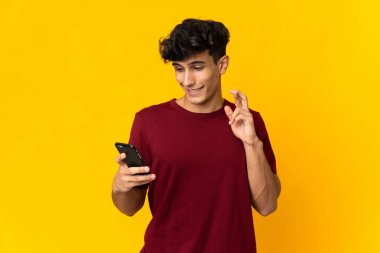 Arjantinli genç adam sarı arka planda parmakları çapraz cep telefonu kullanarak izole edildi