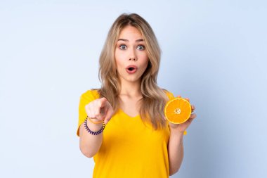 Mavi arka planda portakal tutan genç Rus kız şaşırmış ve ön tarafı işaret ediyor.