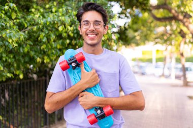 Parkta yüzünde mutlu bir ifadeyle paten yapan beyaz bir genç.