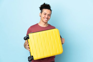 İzole edilmiş mavi geçmişi olan beyaz bir adam seyahat çantasıyla tatilde.