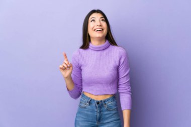 İzole edilmiş mor arka planda genç esmer kadın yukarı bakıyor ve şaşırıyor.