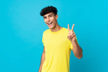 Arjantinli genç adam arka planda izole edilmiş gülümsüyor ve zafer işareti gösteriyor