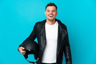 Motosiklet kasklı beyaz bir adam mavi arka planda izole edilmiş ve yüzünde sürpriz bir ifade var.