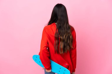 İzole edilmiş pembe arka planda genç bir esmer kız ve arka planda bir paten.