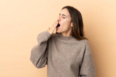 Kafkasyalı genç bir kadın izole edilmiş arka planda esniyor ve geniş ağzını eliyle kapatıyor.