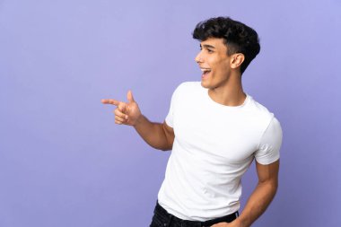 Arjantinli genç bir adam arka planda izole edilmiş bir şekilde parmak ucunda bir ürün sunuyor.