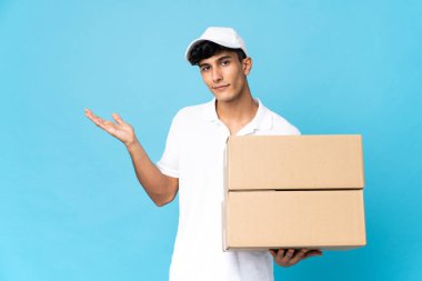 Teslimatçı Arjantinli adam mavi arka planda izole edilmiş. Davet için ellerini yana uzatıyor.