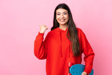 Genç esmer kız izole edilmiş pembe arka planda kayıyor ve yan tarafı işaret ediyor.