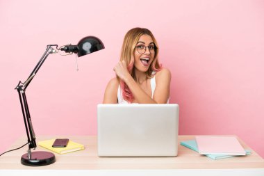 Pembe arka planda dizüstü bilgisayarı olan genç bir bayan öğrenci zaferi kutluyor.