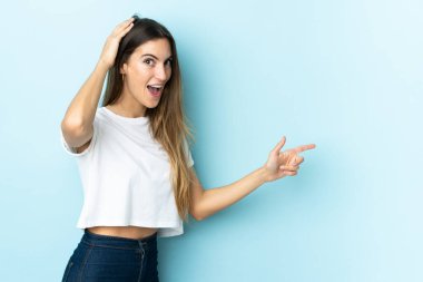 İzole edilmiş arka planda yaşayan beyaz bir kadın şaşırmış ve parmağıyla kenarı işaret ediyor.