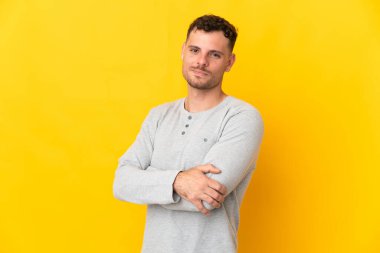 Sarı arka planda izole edilmiş, kolları çapraz ve ileriye bakan beyaz, yakışıklı genç bir adam.