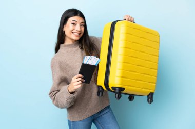 Genç esmer kız izole edilmiş mavi arka planda tatilde bavul ve pasaportla