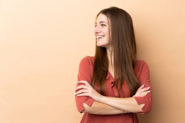 Beyaz tenli genç bir kadın bej arka planda izole edilmiş mutlu ve gülümsüyor.