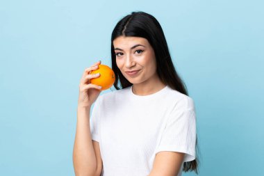 Genç esmer kız izole edilmiş mavi arka planda elinde bir portakal tutuyor.